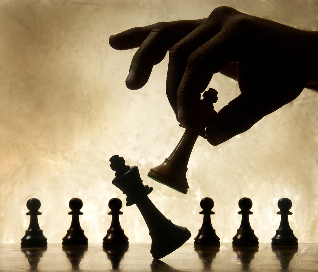 dark hand kicking a chess piece with another on a beige background